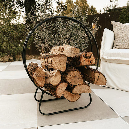 Decor Steals black iron loop fireplace log holder with curved design holding firewood in a cozy fireplace setting