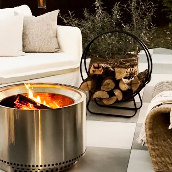 Black iron loop fireplace log holder with curved design, perfect for organizing firewood in a cozy hearth setting.